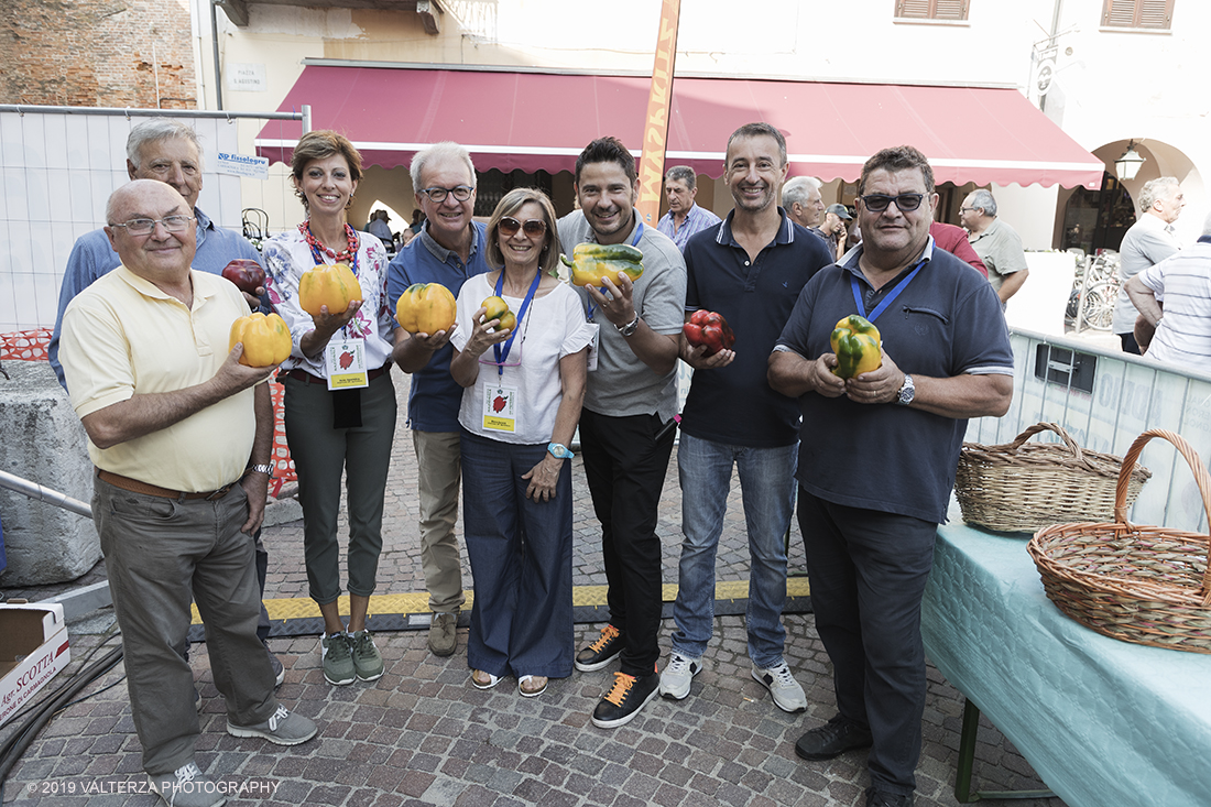 _G3I3082.jpg - 01/09/2019. Carmagnola. TO. Concorso del Peperone  Riservato ai produttori dellâ€™area di coltivazione del Peperone di Carmagnola, si premiano i migliori esemplari i dei quattro ecotipi locali: quadrato, lungo o corno di bue, trottola e tumaticot. Nella foto di gruppo i giudici del concorso con al centro il conduttore della manifestazione nonchÃ¨ titolare di programmi RAI "Tinto"