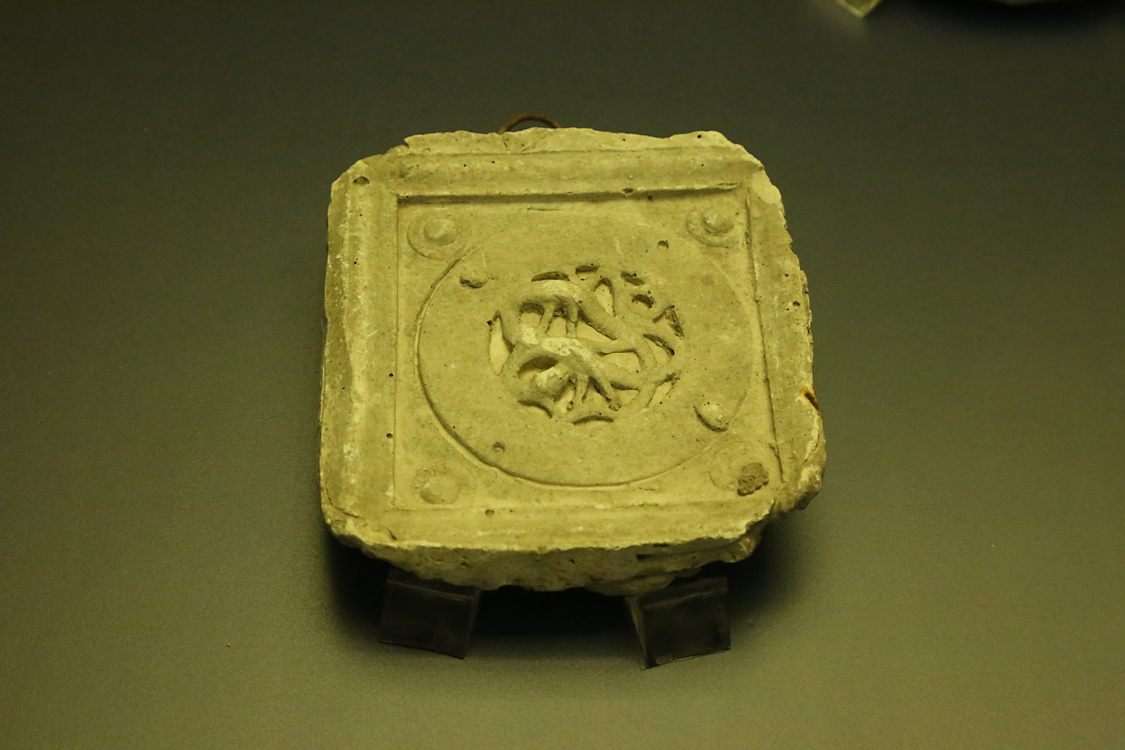 LoScrignoDelCardinale_59.jpg - La bacheca contiene 11 calchi in gesso che riproducono alcuni medaglioni medievali di Limoges --  già decoranti un cofano di Guala Bicchieri — approdati nel XVI secolo a Biella e reimpiegati per impreziosire il coro rinascimentale della chiesa. Vennero realizzati a scopo didattico intorno alla fine dell’Ottocento nei laboratori delle Scuole Professionali di Biella, dal 1873 ospitate nei locali del convento di San Sebastiano. Si tratta di calchi positivi, prodotti senza staccare gli originali dai dossali del coro. Il calco con figura di arpia (prima fila a sinistra, terzo in basso) è il calco del medaglione OA 9475 del Louvre (esposto nella sezione 2, vetrina sud). Nella seconda metà del XIX secolo, nel generale clima di riscoperta del Medioevo, le Scuole di arti e mestieri incentivavano lo studio delle tecniche artistiche medievali, come lo smalto champlevé.