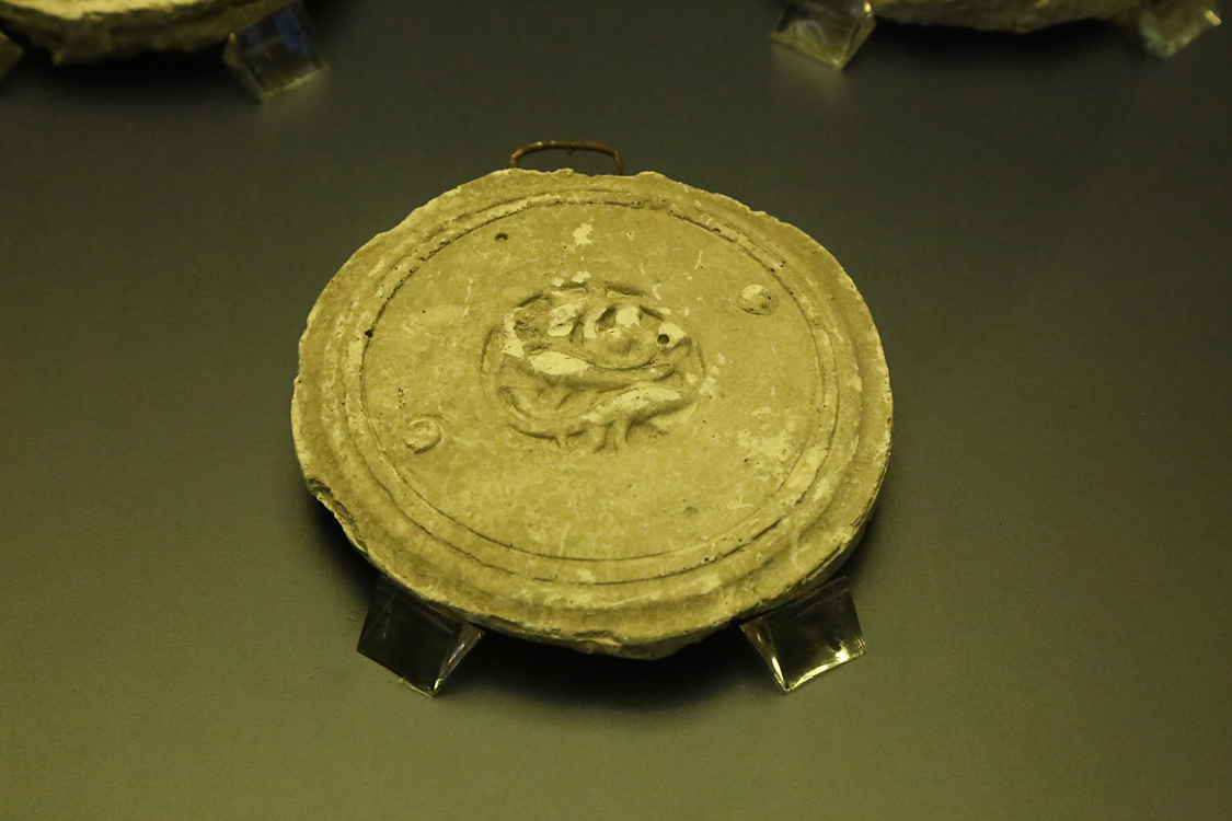 LoScrignoDelCardinale_61.jpg - La bacheca contiene 11 calchi in gesso che riproducono alcuni medaglioni medievali di Limoges --  già decoranti un cofano di Guala Bicchieri — approdati nel XVI secolo a Biella e reimpiegati per impreziosire il coro rinascimentale della chiesa. Vennero realizzati a scopo didattico intorno alla fine dell’Ottocento nei laboratori delle Scuole Professionali di Biella, dal 1873 ospitate nei locali del convento di San Sebastiano. Si tratta di calchi positivi, prodotti senza staccare gli originali dai dossali del coro. Il calco con figura di arpia (prima fila a sinistra, terzo in basso) è il calco del medaglione OA 9475 del Louvre (esposto nella sezione 2, vetrina sud). Nella seconda metà del XIX secolo, nel generale clima di riscoperta del Medioevo, le Scuole di arti e mestieri incentivavano lo studio delle tecniche artistiche medievali, come lo smalto champlevé.