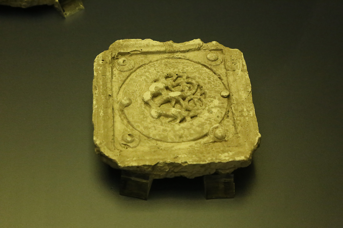 LoScrignoDelCardinale_62.jpg - La bacheca contiene 11 calchi in gesso che riproducono alcuni medaglioni medievali di Limoges --  già decoranti un cofano di Guala Bicchieri — approdati nel XVI secolo a Biella e reimpiegati per impreziosire il coro rinascimentale della chiesa. Vennero realizzati a scopo didattico intorno alla fine dell’Ottocento nei laboratori delle Scuole Professionali di Biella, dal 1873 ospitate nei locali del convento di San Sebastiano. Si tratta di calchi positivi, prodotti senza staccare gli originali dai dossali del coro. Il calco con figura di arpia (prima fila a sinistra, terzo in basso) è il calco del medaglione OA 9475 del Louvre (esposto nella sezione 2, vetrina sud). Nella seconda metà del XIX secolo, nel generale clima di riscoperta del Medioevo, le Scuole di arti e mestieri incentivavano lo studio delle tecniche artistiche medievali, come lo smalto champlevé.