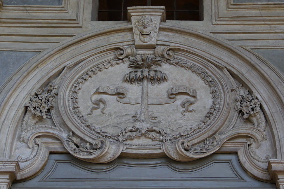 Nuvole_005.JPG - Torino - Palazzo Madama - Scalone d'onore - Medaglione in stucco. E' rappresentato un tronco d'albero attraversato da un cartiglio con la scritta: In Stipite Regnat. E' il motto dei Savoia Carignano, il suo significato letterale dovrebbe essere  "governare in tronco". Infatti  l'immagine del tronco si può associare alla severità, all'inflessibilità e alla fierezza e decoro della reggenza dei savoia.